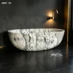 Luxurious marble bathtub with unique veining in a modern bathroom featuring dark stone walls and gold accents.