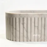 An oval marble sink with a fluted pattern and smooth design, showcasing refined craftsmanship and luxurious material.