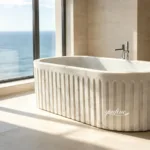 Luxurious modern marble bathtub with sleek fluted design placed near a window overlooking the ocean in a bright bathroom.
