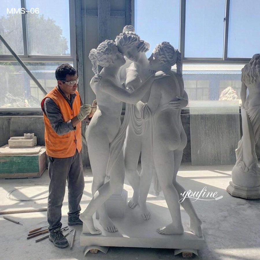 An artisan wearing an orange vest meticulously carving a detailed marble sculpture of three intertwined figures in a workshop.