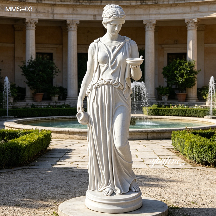Elegant white marble statue of a woman holding a bowl and pitcher, placed near a circular fountain surrounded by hedges and classical columns.