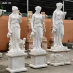 Three elegantly carved marble goddess statues on pedestals displayed outdoors, surrounded by other sculptures.