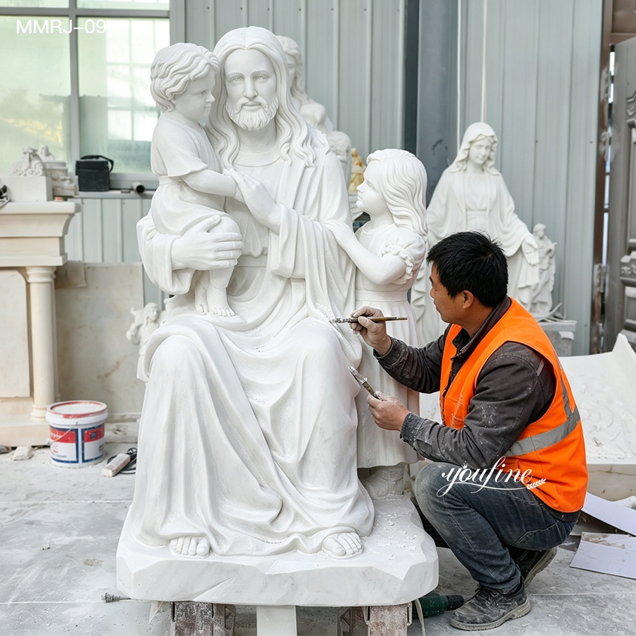 Sculptor wearing an orange vest working on a white marble religious statue featuring a seated figure with two children.
