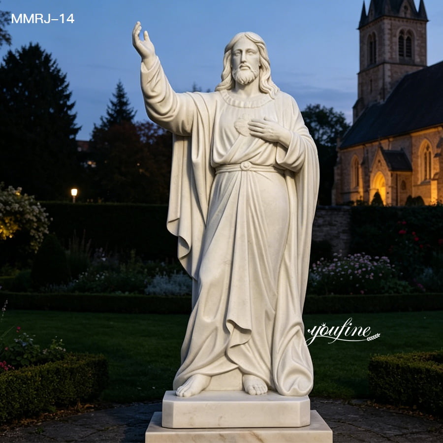 A white marble statue of Jesus with an outstretched arm standing in an evening garden, with a lit church in the background.