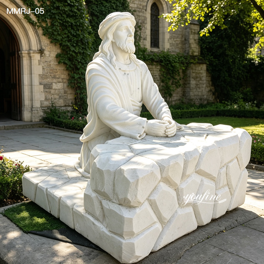 Detailed marble sculpture of Jesus praying at a stone altar, positioned outdoors near a stone building with ivy and greenery.