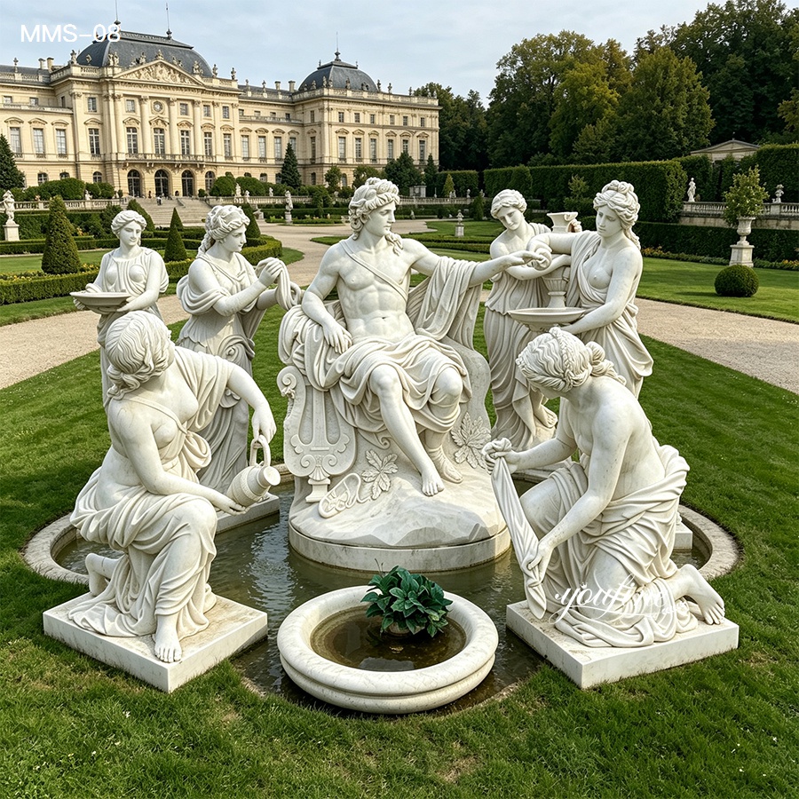 Elegant marble sculpture group depicting classical figures placed within a landscaped garden in front of a grand palace building.