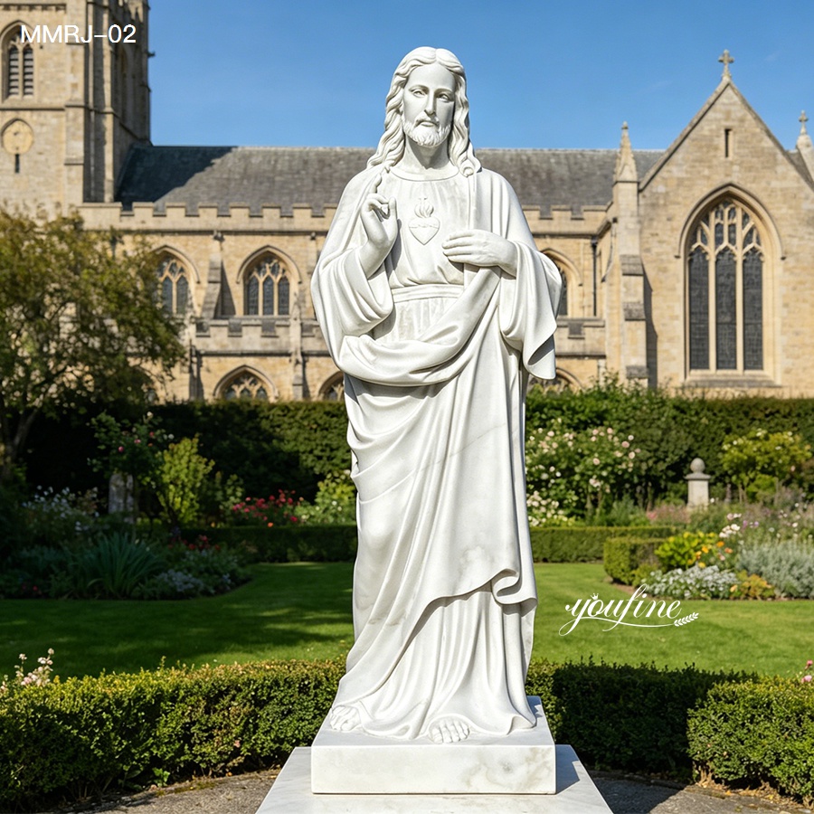 White marble statue of the Sacred Heart of Jesus in a landscaped garden with a historic stone church in the background on a sunny day.