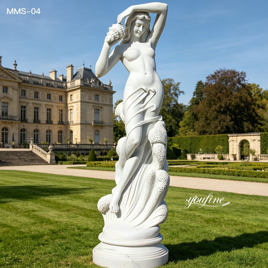 A refined white marble sculpture of a woman holding a shell, positioned outdoors in a landscaped garden with a grand building in the background.