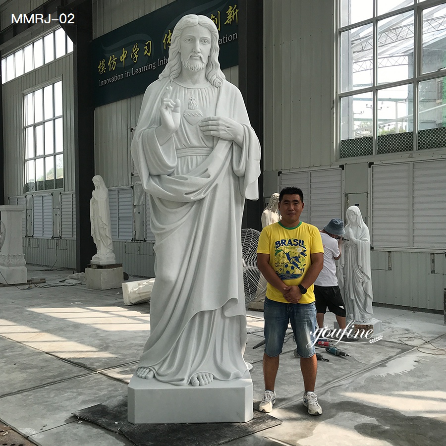 White marble statue of Jesus Christ with Sacred Heart, displayed in a workshop alongside a person standing nearby.