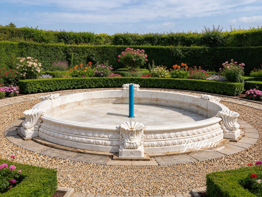 Ornate marble fountain base with intricate carvings set in a beautifully landscaped garden surrounded by hedges and flowers.