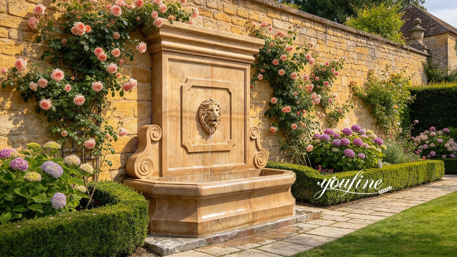 A luxurious marble wall fountain with a lion head design set against a stone wall, surrounded by blooming roses and hedges.